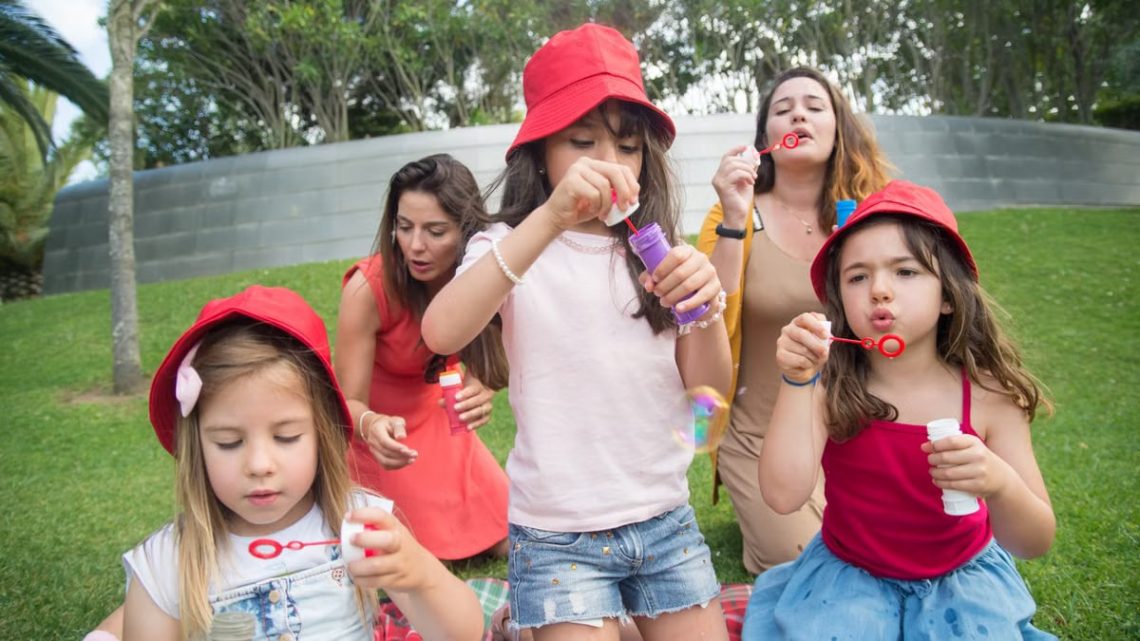 Happy children and adults enjoying bubble-blowing in a sunny park, creating joyful summer memories.